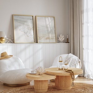 May include: Two framed beach scene prints with a white wicker coffee table and two white chairs with a straw hat on one. The coffee table has a gold candle holder and a beaded garland.