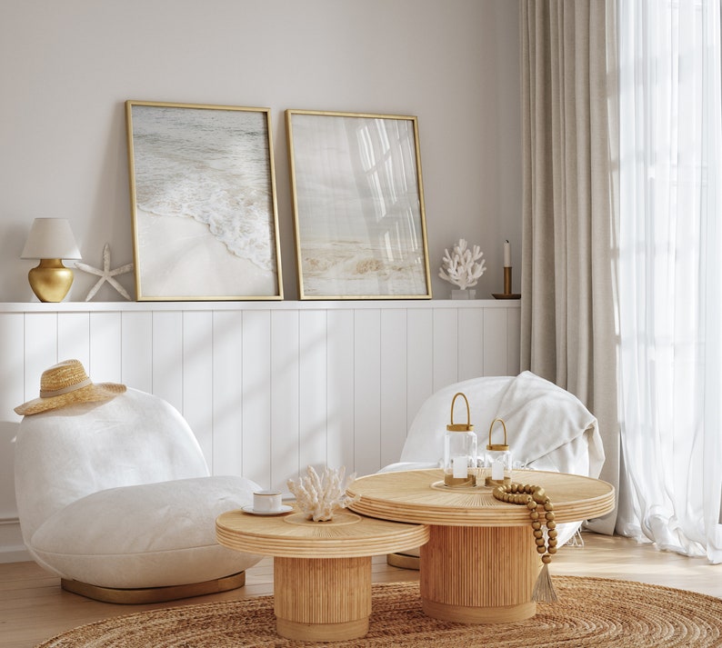 May include: Two framed beach scene prints with a white wicker coffee table and two white chairs with a straw hat on one. The coffee table has a gold candle holder and a beaded garland.
