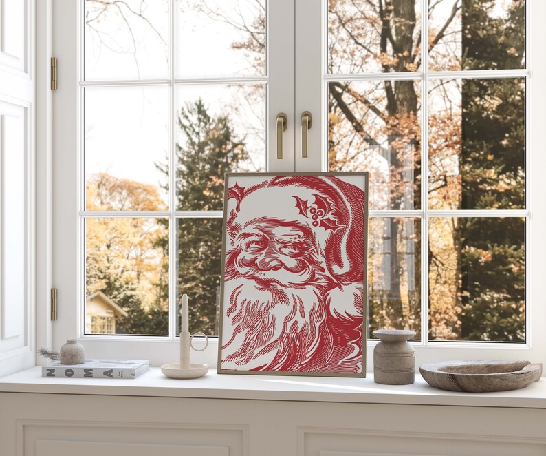 K&ouml;nnte beinhalten: Eine rote und wei&szlig;e Illustration von Santa Claus' Gesicht mit einem Stechpalmenzweig auf seinem Hut. Die Illustration ist gerahmt und h&auml;ngt an einer Wand.