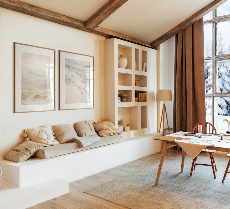 May include: A living room with a white couch, a wooden table, and a large window with a view of a snowy forest. The room is decorated with a brown rug, a lamp, and two framed pictures of seascapes.