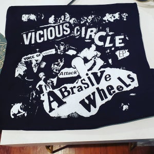Pode incluir: Design gr&aacute;fico preto e branco em uma camiseta preta. O design apresenta o texto "Vicious Circle EP" e "The Abrasive Wheels" com um nome de banda "Voice of Youth" e "Attack" em texto menor.