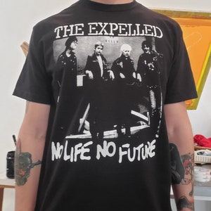 Pode incluir: Camiseta preta com uma estampa gráfica branca de uma banda chamada "The Expelled" com o texto "No Life No Future" abaixo do nome da banda.