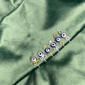 May include: Five gold and silver wire hair clips with blue and white evil eye charms. The charms are attached to the wire with a loop.