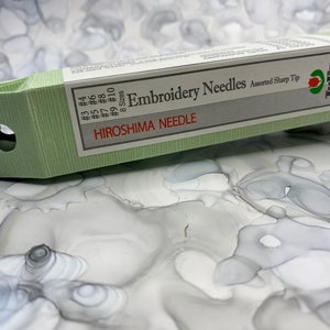 May include: A green box of Tulip embroidery needles with a red string attached. The box is labeled "Hiroshima Needle" and "Embroidery Needles Assorted Sharp Tip". The box contains 8 sizes of needles, from #3 to #10.
