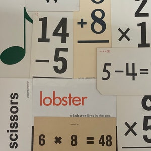 May include: A collection of flashcards with various math problems and words, including "scissors", "lobster", "14 + 8", "5 - 4", "6 x 8 = 48", and "2 x 1".