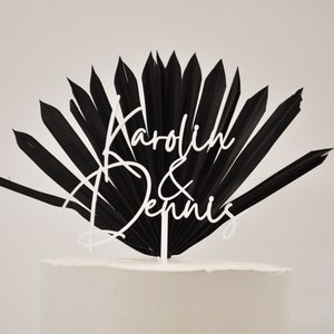 May include: Black palm leaf cake topper with white script lettering that reads "Karolin & Dennis".