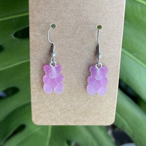 K&ouml;nnte beinhalten: Ein Paar Ohrringe mit einem rosa Gummib&auml;rchen-Anh&auml;nger. Die Ohrringe haben silberne Haken.