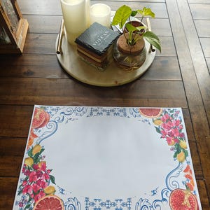 Puede incluir: Una mesa de madera con una bandeja decorativa con velas, posavasos y una pequeña planta. Una alfombrilla con un diseño floral y de frutas está sobre la mesa. La alfombrilla tiene un centro blanco con un borde de flores rojas, limones y granadas.