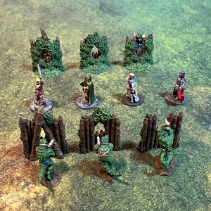 May include: Miniature fantasy game figures and terrain pieces. The scene includes several small figures, green terrain pieces, and wooden fence-like structures. The figures are painted with various colors and details, suggesting a tabletop role-playing game setting.
