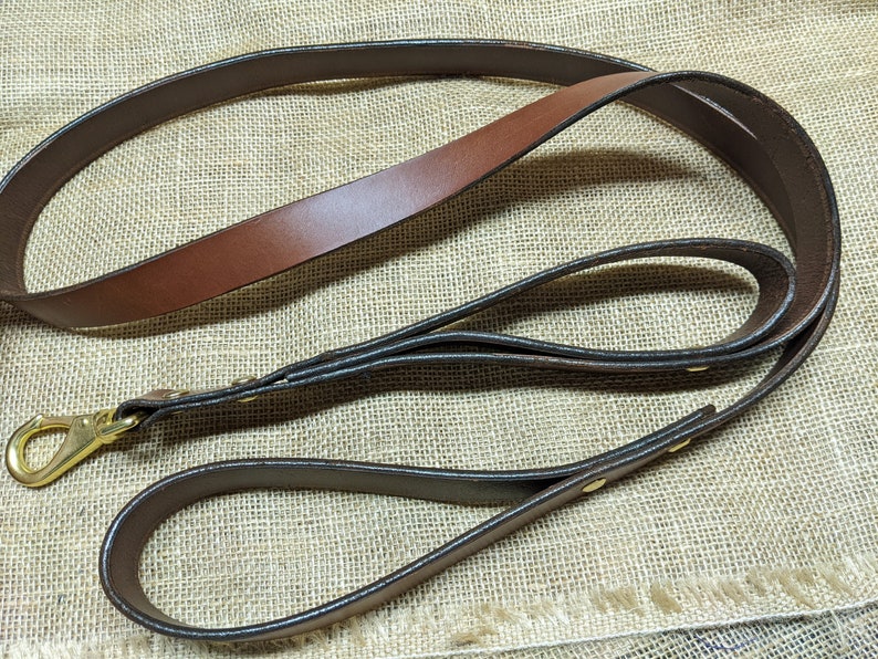 Peut inclure: Une laisse de chien en cuir marron avec une boucle en laiton. La laisse est pli&eacute;e en deux et a une double couche de cuir.