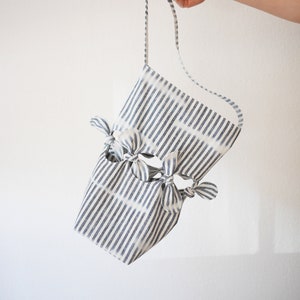 May include: A white and blue striped tote bag with knotted handles. The bag is made of fabric and has a casual, relaxed style.