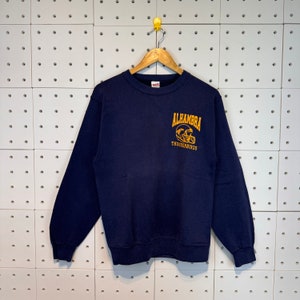 May include: A navy blue sweatshirt with a gold embroidered logo that says "Alhambra Thunderbirds" and features a football helmet.