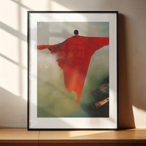 以下が含まれることがあります： 赤いマントを着た人が空を飛んでいる絵の額装されたプリント。背景はぼんやりとした緑と茶色です。