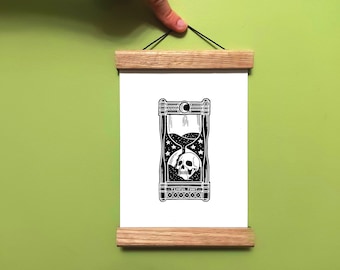 May include: A white rectangular print featuring a black ink illustration of an hourglass containing a skull, stars, and the text "TEMPUS FUGIT". The print is held by two horizontal light brown wooden magnetic bars with a black string for hanging.