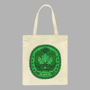 May include: A beige tote bag with a green circular design featuring a stylized face with a beard and the text "The Green Man".