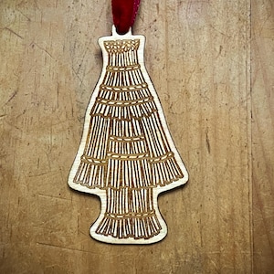 May include: A wooden Christmas tree bauble with a brown and white design. The bauble is shaped like a Christmas tree and has a red ribbon attached to the top.