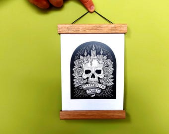 May include: A rectangular wall hanging featuring a black and white print of a skull surrounded by roses and candles, with the text MEMENTO MORI on a banner. The print is held by two light-colored wooden magnetic bars and a black hanging string.
