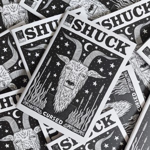 May include: A stack of black and white zines with the title "SHUCK CURSED" printed on the cover. The cover features a goat with horns and a crescent moon in the background.