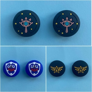 May include: Four different coloured and designed video game controller caps. Two are blue with a white shield design, one is dark blue with a yellow and black design, and one is dark blue with a pink and blue eye design.