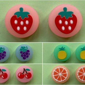 May include: Eight colourful silicone button caps featuring various fruit designs: a strawberry, grapes, a pineapple, a cherry, and an orange slice. The caps are designed for use with gaming controllers.