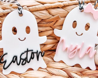 May include: Two white ghost-shaped ornaments with black and white twine hangers. One ghost features the black script name Easton, while the other features the pink script name Myla and a small pink bow attached to the top of its head.