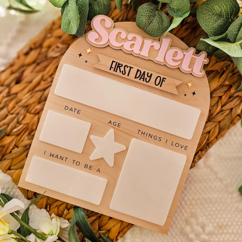 May include: Wooden first day of school sign with the name "Scarlett" in pink. The sign includes spaces for the date, age, and things I love. The text "FIRST DAY OF" is also visible.