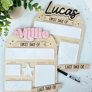 May include: Two wooden first and last day of school boards. One board has the name "Lucas" in black script, the other has "Millie" in pink. Both boards have space for date, age, and things I love.