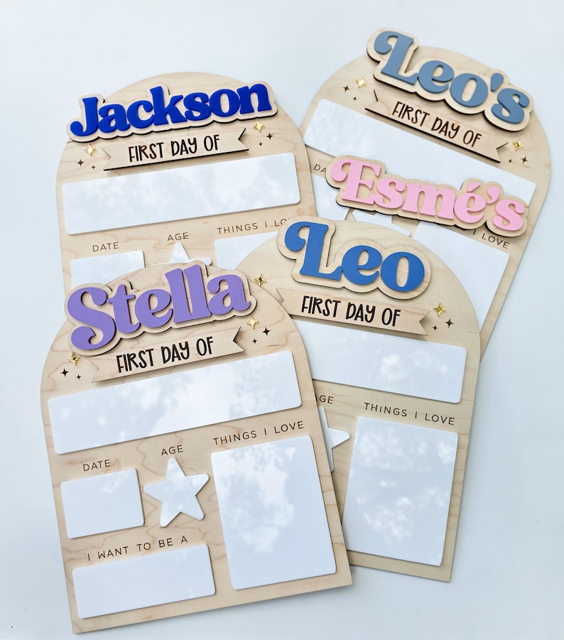 May include: Wooden first day of school signs with the names Jackson, Leo's, Esme's, Stella, and Leo in colorful 3D lettering. Each sign has space for date, age, and things they love. The signs are decorated with star and sparkle accents.