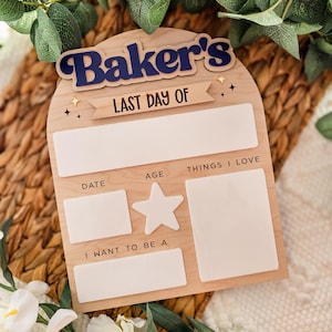 May include: Wooden sign with the text "Baker's LAST DAY OF" in navy blue and white. The sign has spaces for "DATE", "AGE", "THINGS I LOVE", and "I WANT TO BE A". A star-shaped cutout is also included.