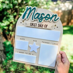 May include: A wooden sign with the name "Mason" in teal script. The sign includes the text "FIRST DAY OF" and spaces for date, age, and "THINGS I LOVE." There is also a star and a space for "I WANT TO BE A."