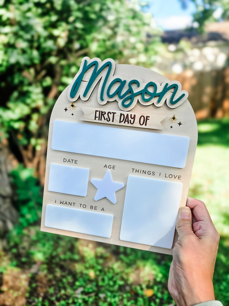 May include: A wooden sign with the name "Mason" in teal script. The sign includes the text "FIRST DAY OF" and spaces for date, age, and "THINGS I LOVE." There is also a star and a space for "I WANT TO BE A."