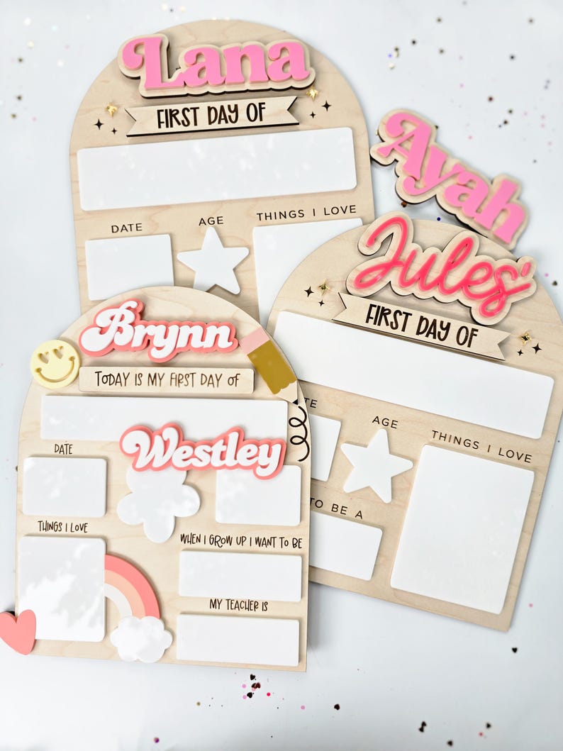 May include: Wooden first day of school boards with names in pink and white. Each board has space for the date, age, and things they love. Additional boards include a rainbow, clouds, and a pencil.