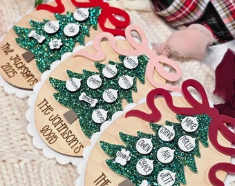 May include: Christmas tree ornaments made of wood, featuring family names and the year 2025. Each has a green glitter tree, white scalloped edges, and a decorative bow. Names are on white circular tags.