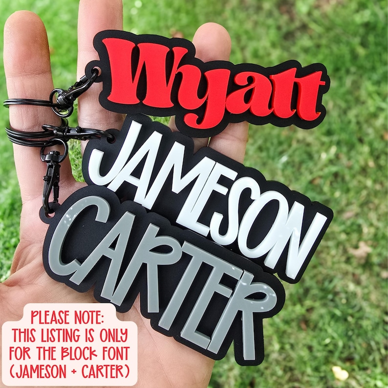 May include: Three custom keychains with black bases and raised lettering. The top keychain features the red name Wyatt, the middle has the white name JAMESON, and the bottom has the grey name CARTER. Each includes a black metal ring and clip.