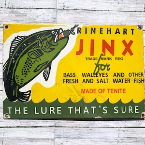 May include: Vintage metal sign with a yellow background and a green fish illustration. The sign reads "RINEHART JINX" and "THE LURE THAT'S SURE." It is designed for bass, walleyes, and other fresh and saltwater fish.