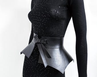 May include: A black sequined top with a wide black leather belt featuring a bow detail. The belt has a pointed, flared shape.