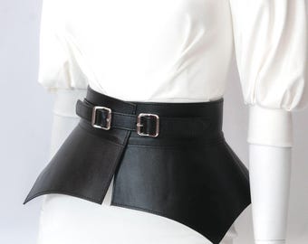 May include: A black leather belt with two silver buckles and a wide, pointed,  flared bottom. The belt is worn over a white shirt.