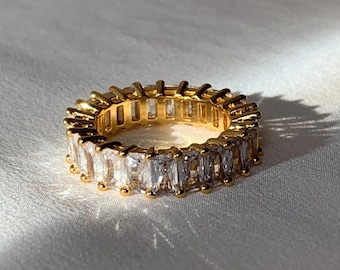 May include: A gold ring with a row of clear baguette-shaped stones.