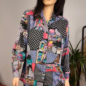 Op de afbeelding: Een lang mouw overhemd met knopen en een geometrische print in tinten roze, blauw, groen, geel en bruin. Het overhemd heeft een zwarte achtergrond met witte stippen.