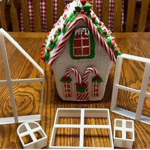 May include: A festive gingerbread house with candy cane decorations and a red and green roof, alongside white plastic window frame moulds. The house has candy cane details and a holiday theme.