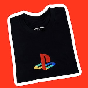 May include: Black t-shirt with a red, yellow, blue, and green embroidered PlayStation logo. The text "OREJAMESO" is embroidered on the shirt.