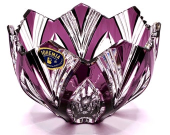 May include: A deep purple and clear cut crystal bowl featuring a jagged, star-like rim and vertical geometric facets. A blue and gold sticker on the side reads BOHEMIA CZECHOSLOVAKIA CRYSTAL OVER 24% PBO. The bowl has a heavy, reflective glass construction.