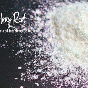 May include: A close-up of a pile of white-red interference mica pigment. The pigment has a pearlescent sheen and is labeled "Galaxy Red".