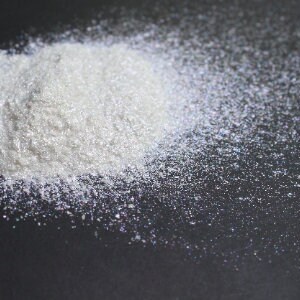 Puede incluir: Un mont&oacute;n de purpurina blanca iridiscente sobre una superficie negra. La purpurina est&aacute; dispersa alrededor del mont&oacute;n, creando un efecto brillante.