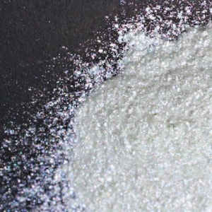 Puede incluir: Primer plano de polvo de purpurina blanco iridiscente sobre un fondo negro.