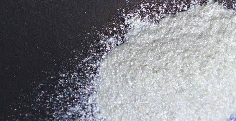 Puede incluir: Primer plano de polvo de purpurina blanco iridiscente sobre un fondo negro.