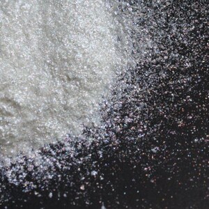 Puede incluir: Un mont&oacute;n de purpurina blanca iridiscente sobre un fondo negro. La purpurina es muy fina y tiene un brillo nacarado.