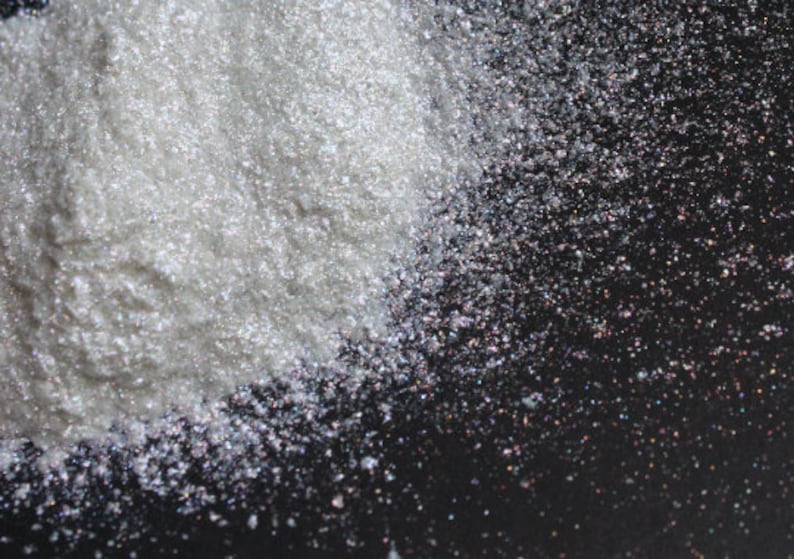 Puede incluir: Un mont&oacute;n de purpurina blanca iridiscente sobre un fondo negro. La purpurina es muy fina y tiene un brillo nacarado.