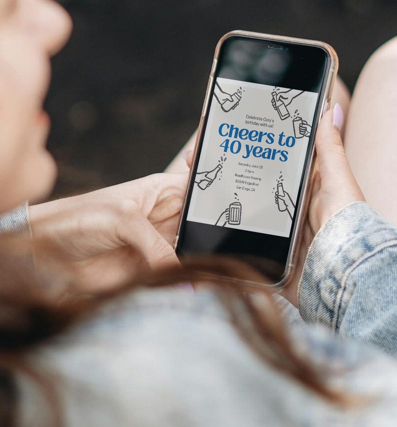 May include: A smartphone displays a birthday invitation with the text "Cheers to 40 years" in blue. The invitation includes line drawings of hands holding bottles and mugs. The phone is held by a person wearing a denim jacket.
