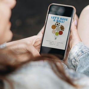 May include: A smartphone displays a sports-themed birthday party invitation. The invitation features a cluster of balloons shaped like sports balls, with the text "LET'S HAVE A BALL!" in blue. Additional text provides party details.